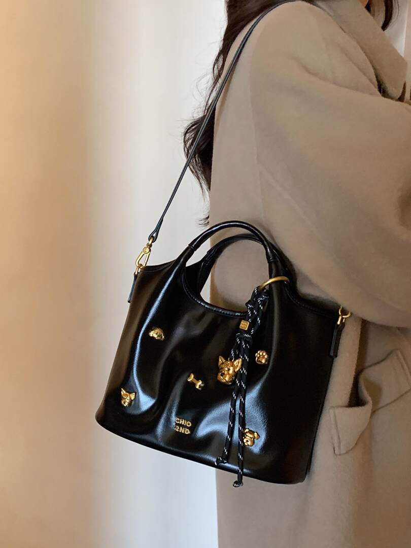 Black leather shoulder handbag with gold charm accents worn by a model