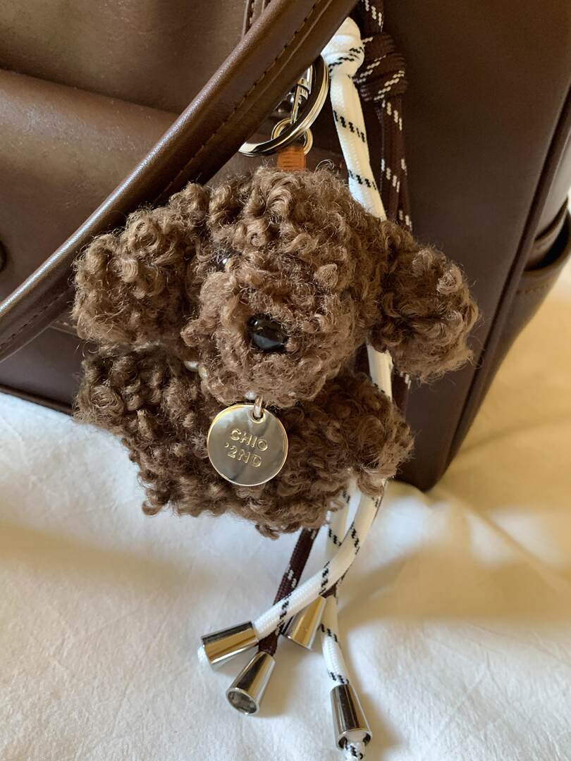 Brown curly dog bag charm hanging from a handbag strap