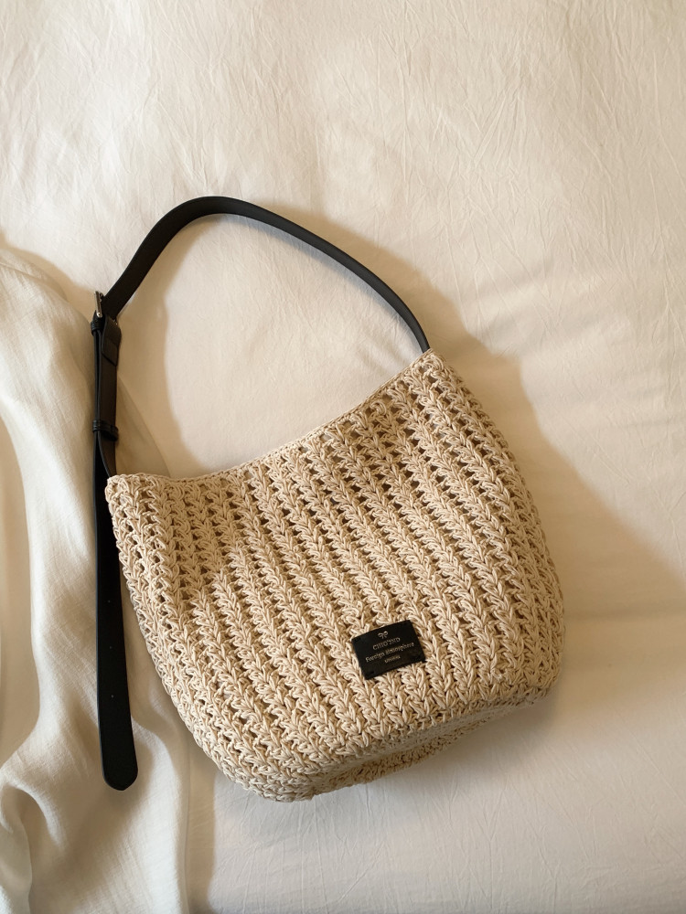 Beige woven shoulder bag with a black strap on a light fabric background