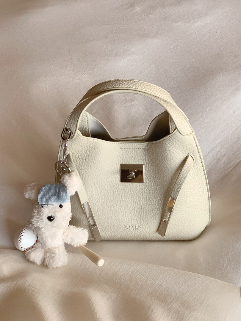 Cream textured leather handbag with a top handle and charm accessory
