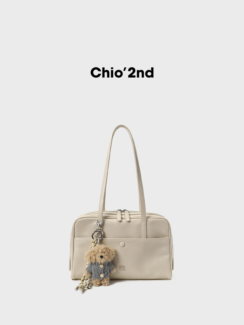 Beige structured handbag with a teddy bear charm on a white background