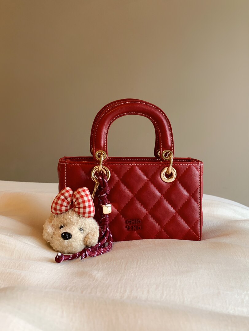 Red quilted handbag with a teddy bear charm on a bed