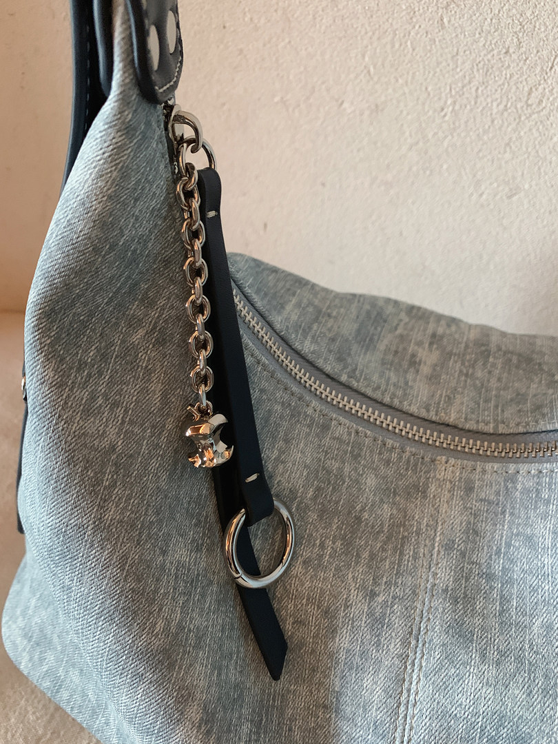 Close-up of a light blue denim shoulder bag with chain charm