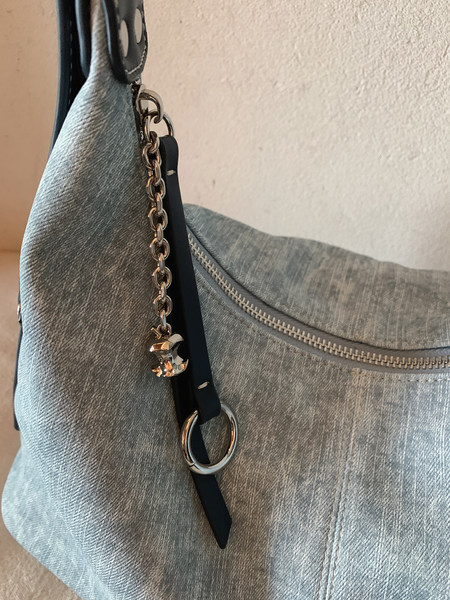 Close-up of a light blue denim shoulder bag with chain charm