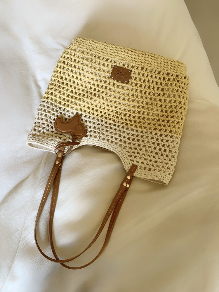 Cream woven handbag with brown leather straps on a white background