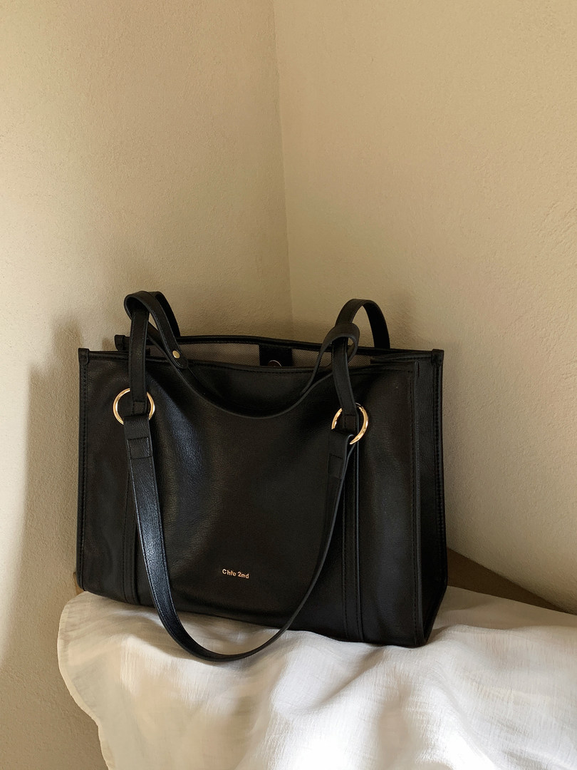 Black leather tote bag with long shoulder straps on a bed