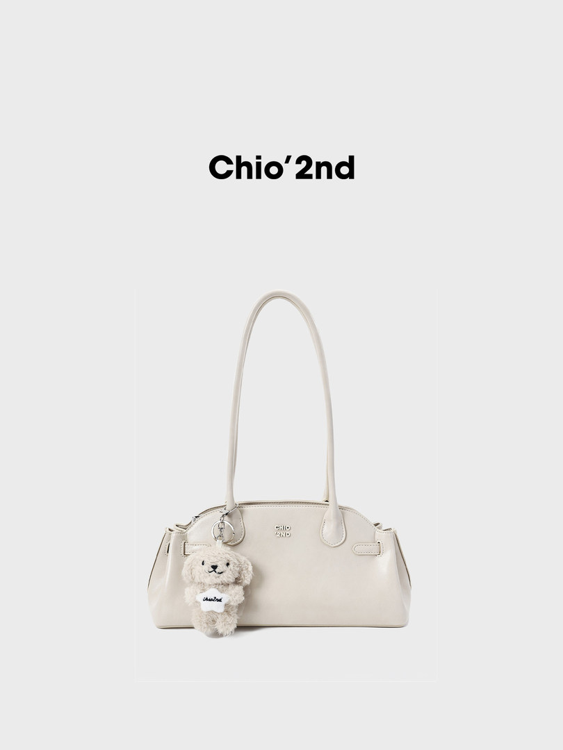 Cream shoulder handbag with teddy bear charm on a white background
