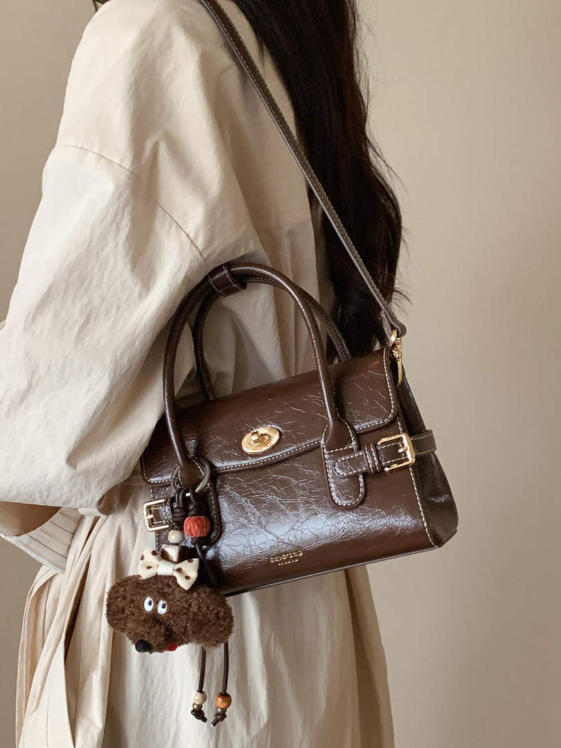 Brown leather handbag worn crossbody with decorative charm