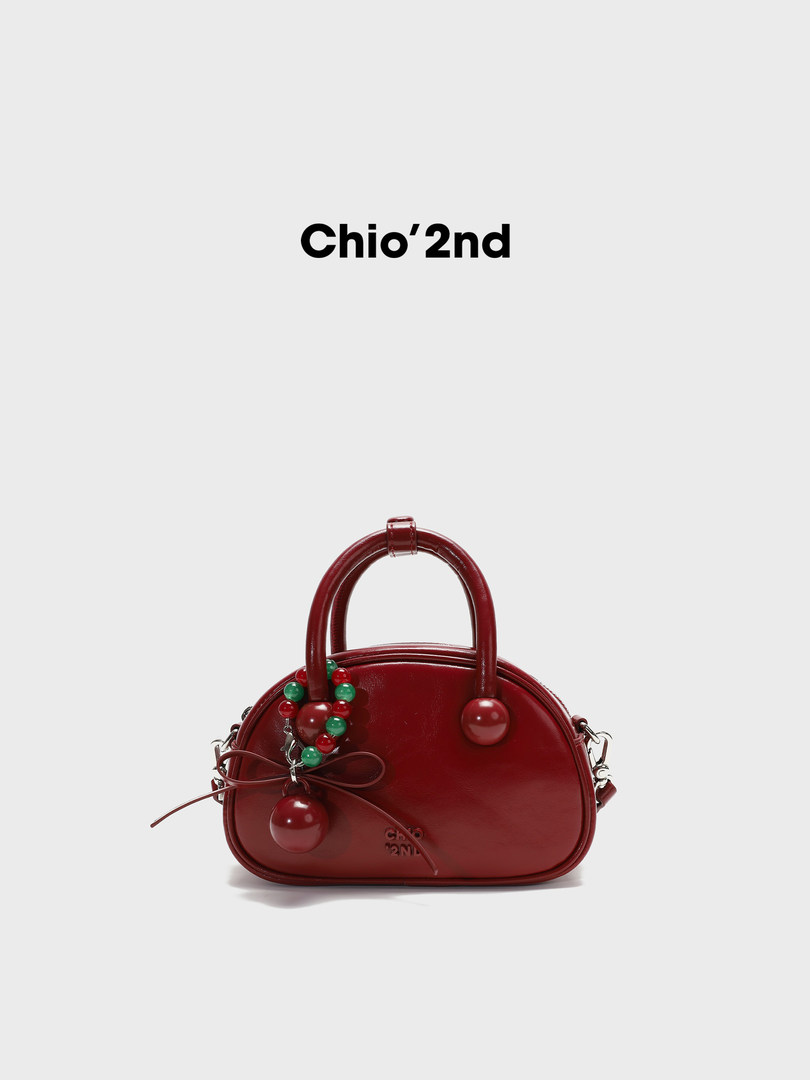Red leather handbag with decorative berry charm and bow detail on a white background