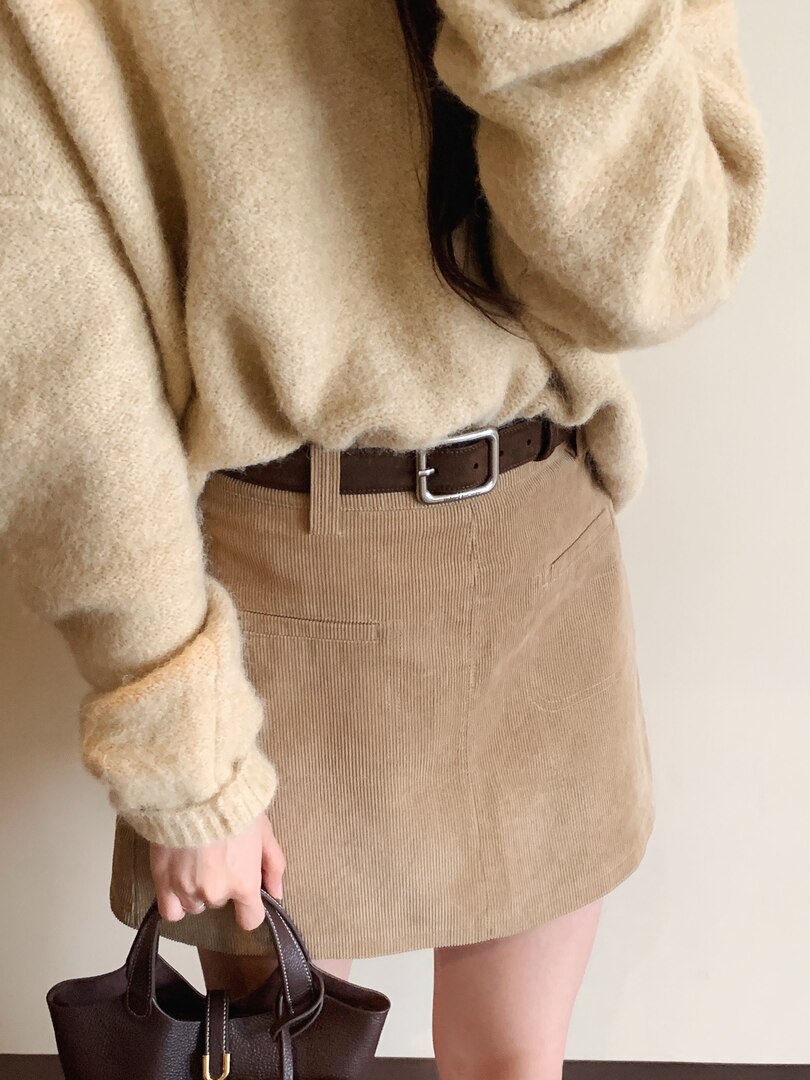 Model wearing a beige knit sweater with a tan corduroy mini skirt, brown belt, and handbag