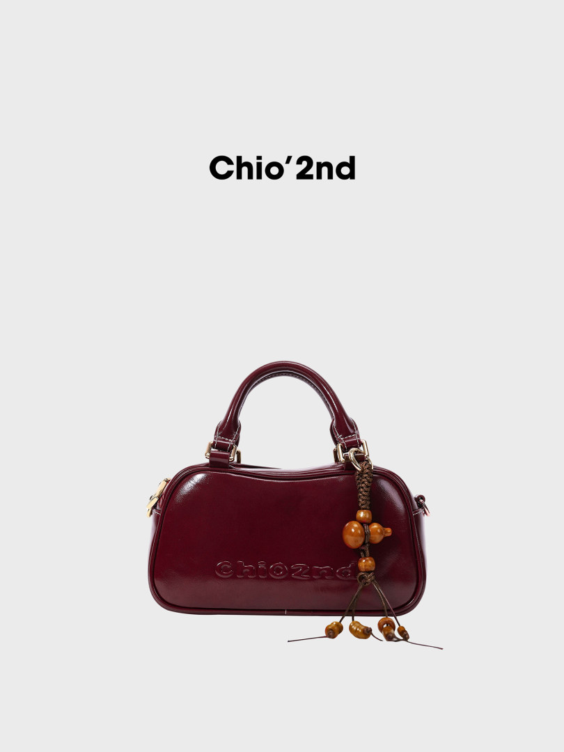 Burgundy structured handbag with top handle and decorative charm