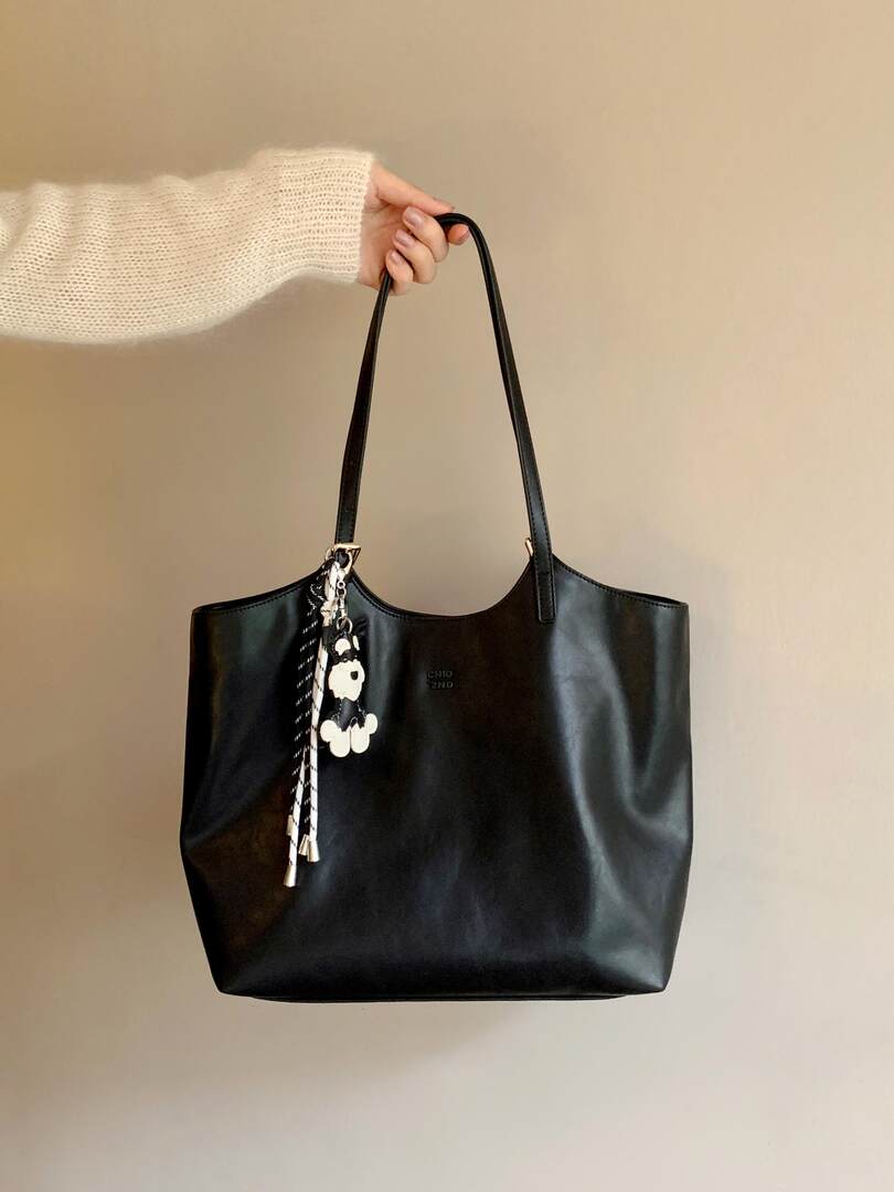 Black tote handbag with long straps being held by hand
