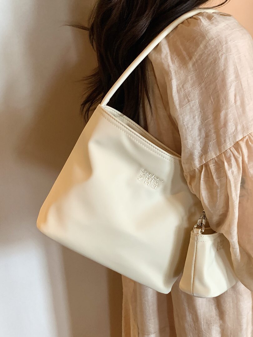 Cream shoulder bag worn over a beige dress
