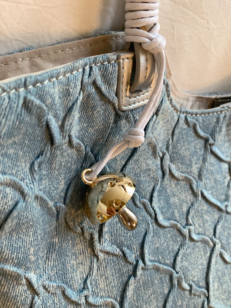 Close-up of a blue denim bag with drawstring and gold heart-shaped charm