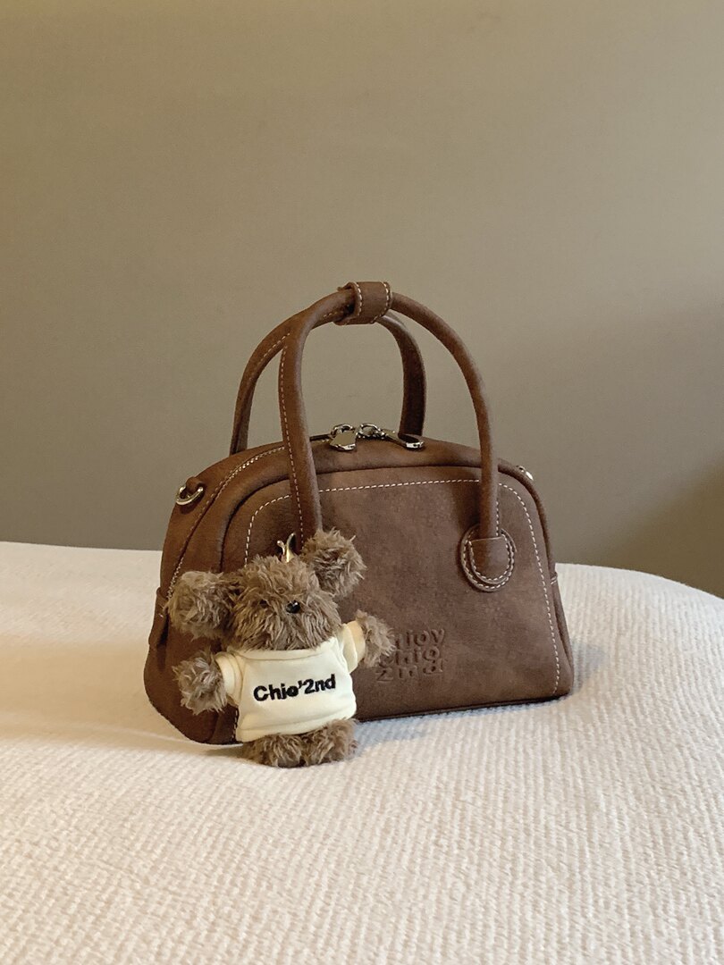 Brown leather handbag with curved top handles and a small teddy bear accessory