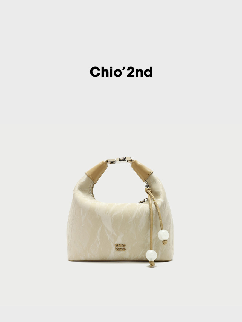 Beige leather handbag with top handle and charm detail on white background