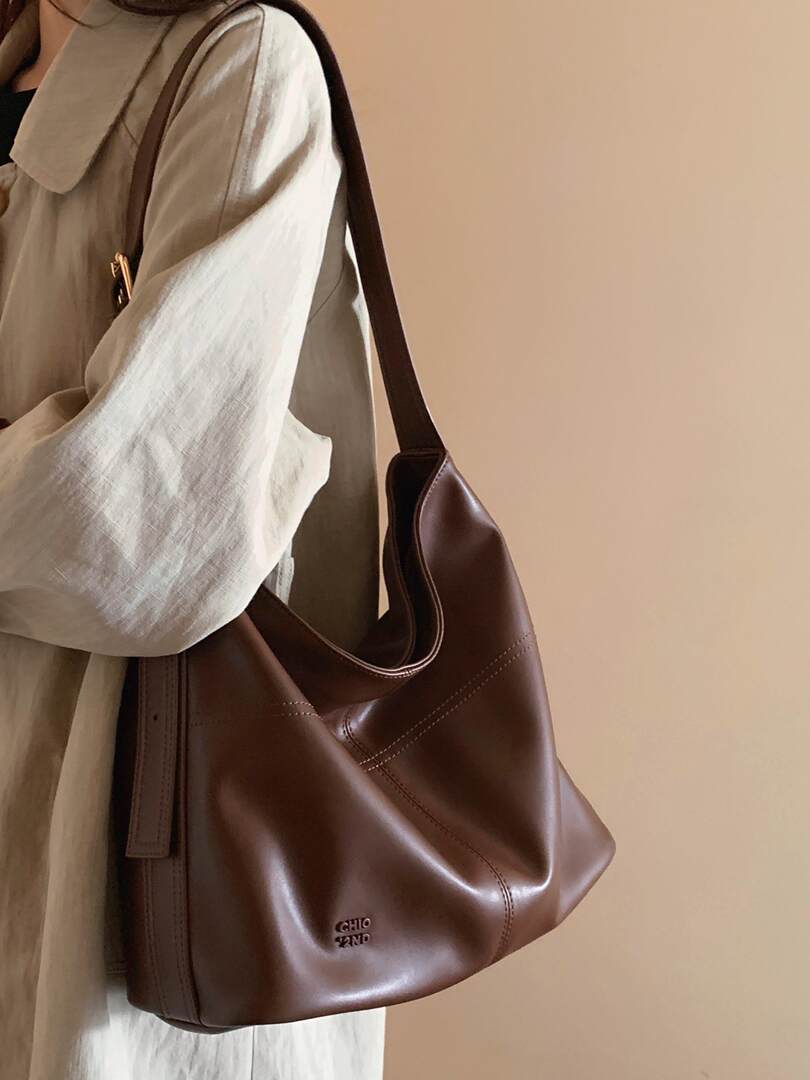 Brown leather shoulder bag worn by a person in a neutral outfit
