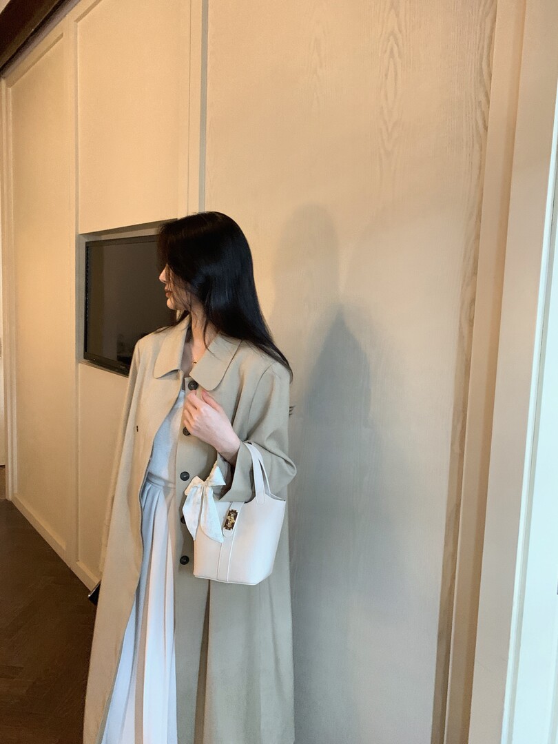 Woman wearing a beige long coat over a white dress and carrying a white handbag