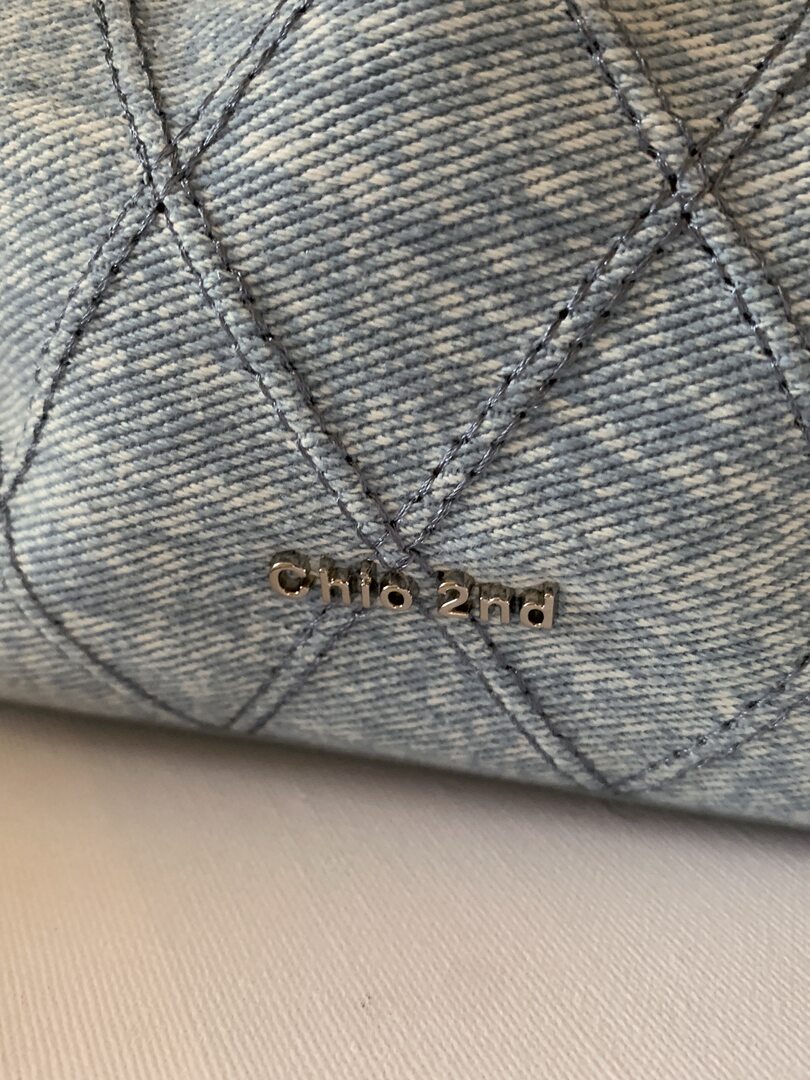 Close-up of a light blue denim product with stitched pattern and metallic "chic 2nd" logo