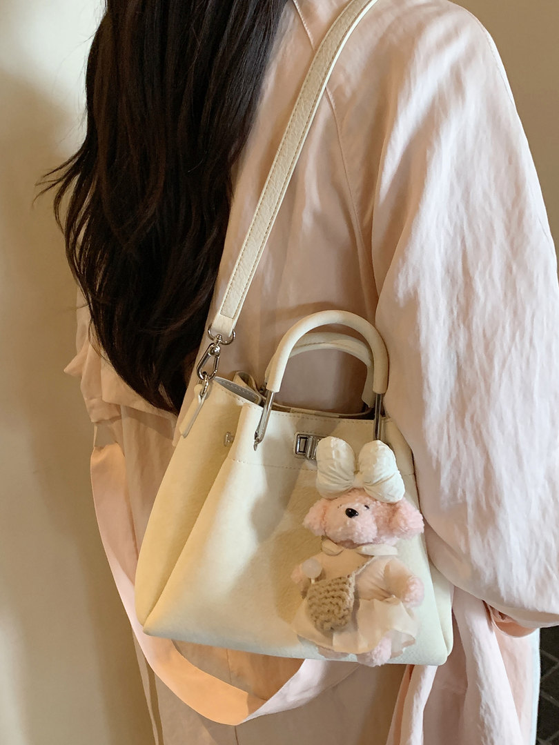 Cream shoulder handbag with teddy bear charm being worn by a model