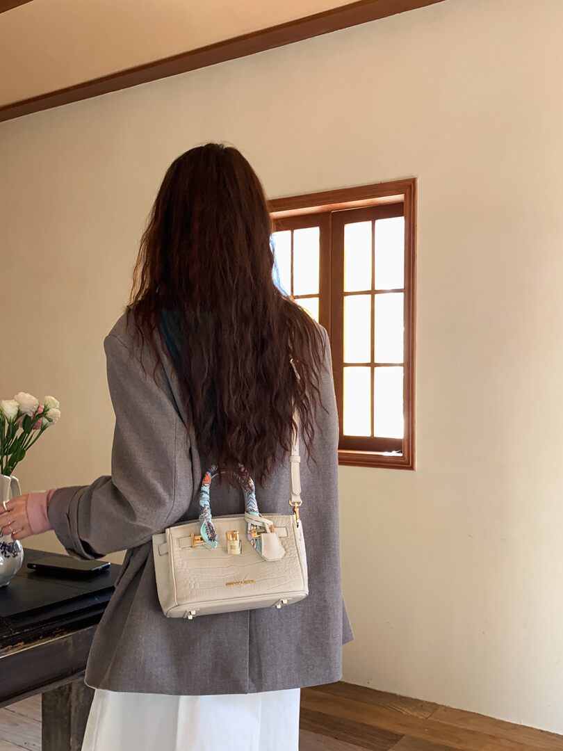 Cream crocodile-texture handbag worn on a model's back with scarf-wrapped handles