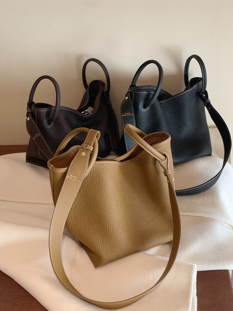 Three textured leather tote handbags in black, brown, and tan on a fabric surface