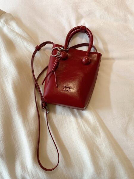 Red leather handbag with shoulder strap on fabric background
