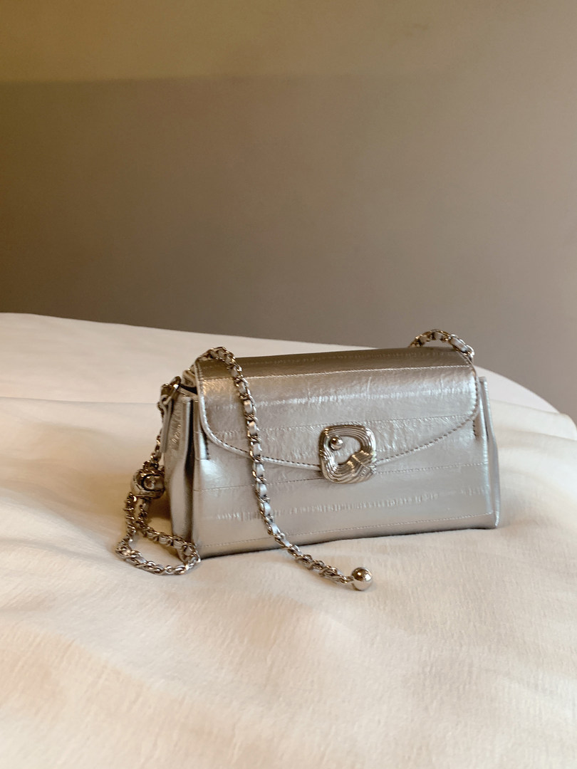 Silver chain-strap handbag displayed on a bed