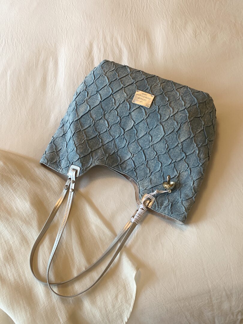 Blue textured shoulder bag with long straps laid on fabric