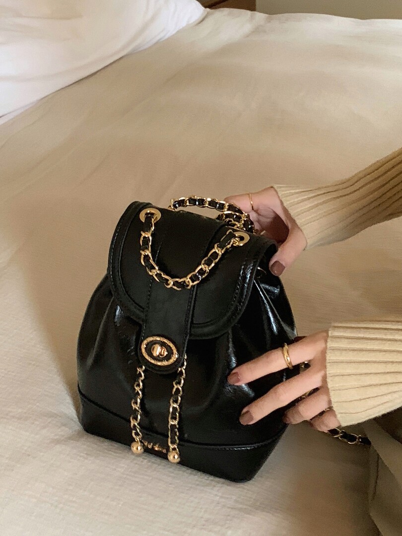 Black leather handbag with gold chain detail being held in hand