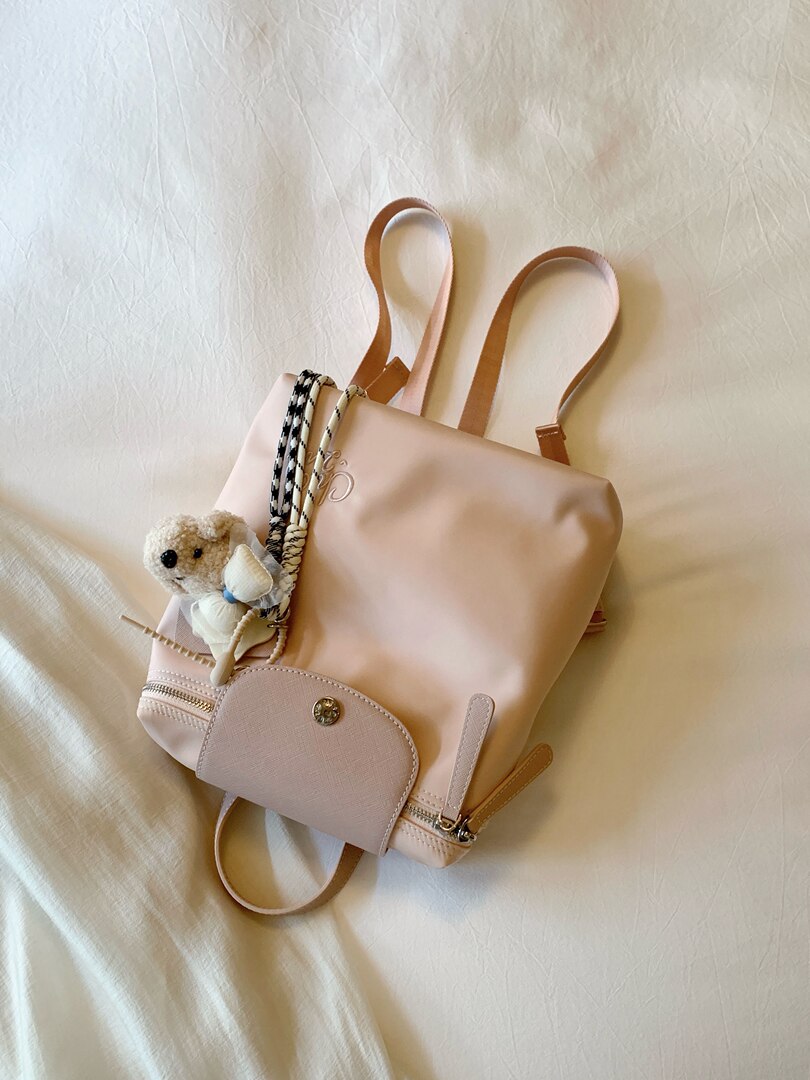 Light pink backpack purse with decorative charms on a white background