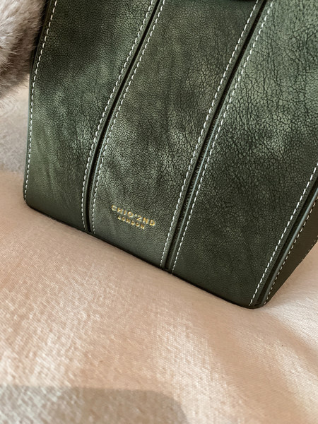 Close-up of a green leather handbag with stitched panels and gold logo