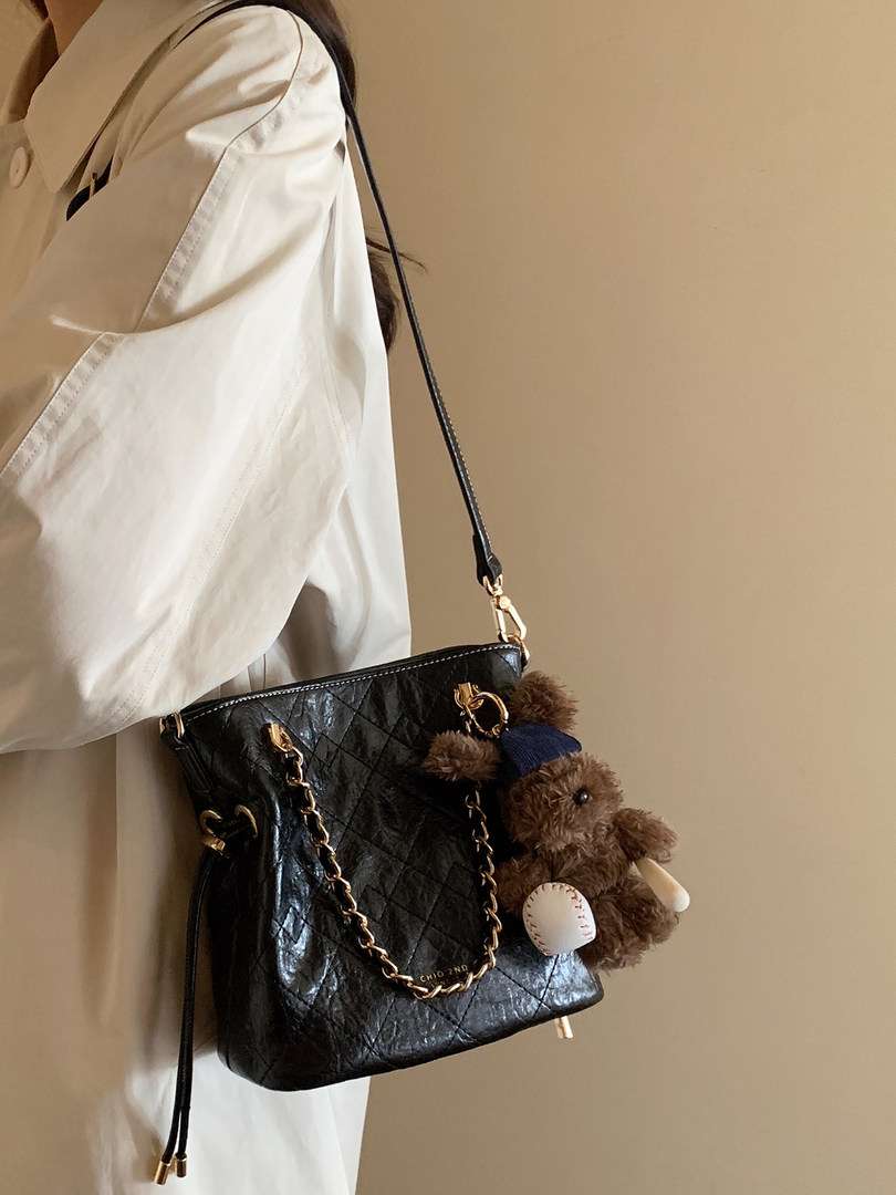 Black quilted chain-strap handbag worn crossbody with a teddy bear charm