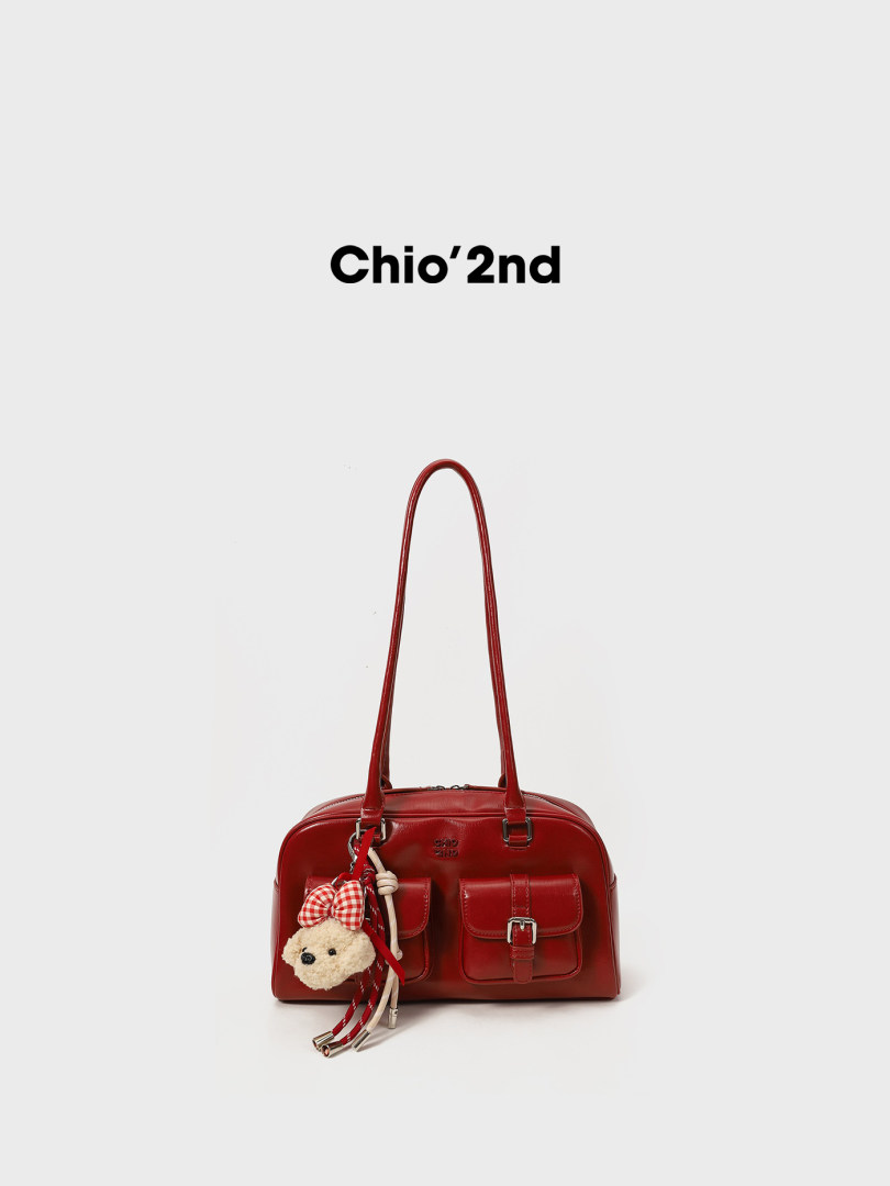 Red leather handbag with long shoulder straps and a plush charm on a white background