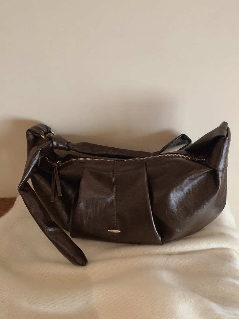Dark brown leather handbag with zipper detail on a bed