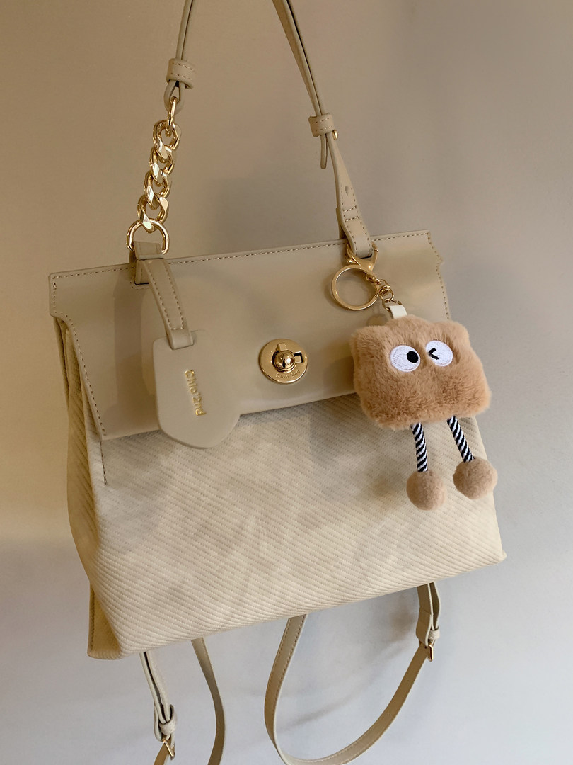 Beige structured handbag with gold chain strap and fuzzy keychain charm