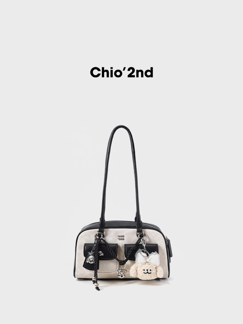 Black and beige handbag with long handles and decorative charms on a white background
