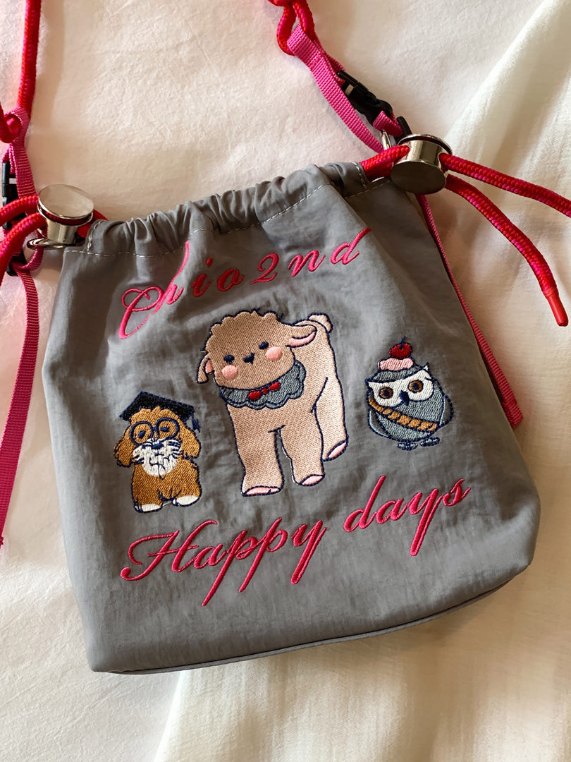 Gray drawstring pouch with pink cords and embroidered cartoon animals and text