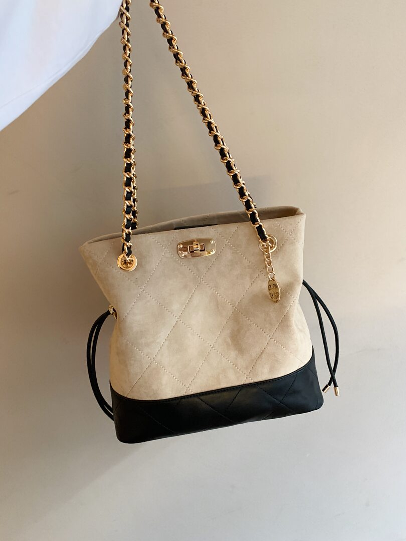 Two-tone quilted handbag with gold chain strap on plain background