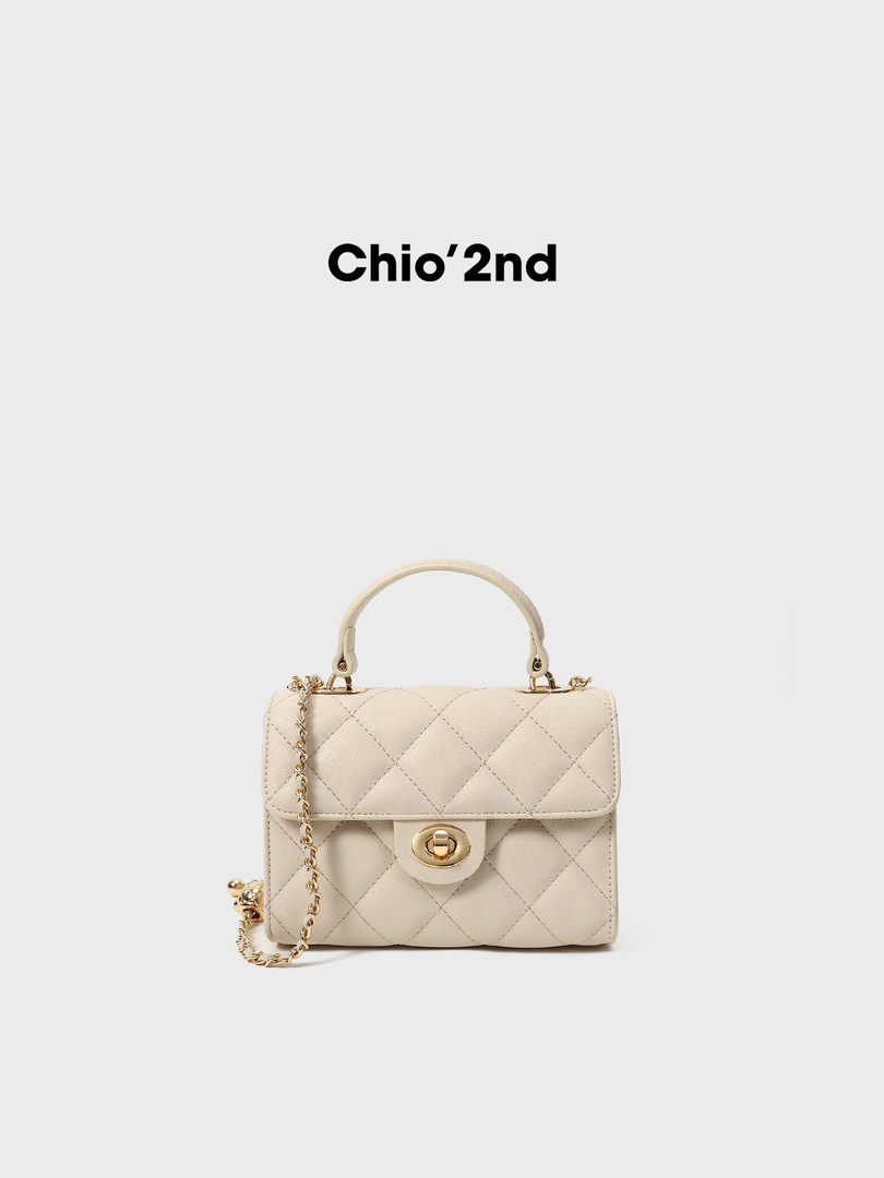 Cream quilted handbag with top handle and gold chain strap on a plain background