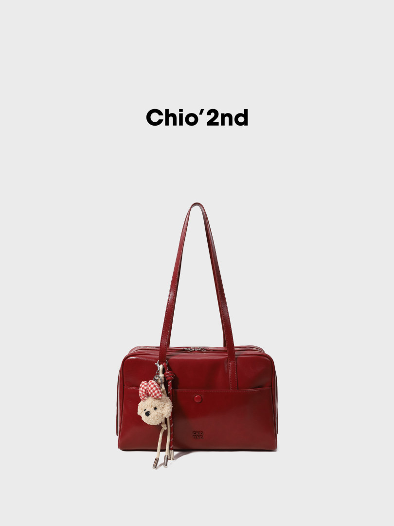 Red leather shoulder handbag with a teddy bear charm on a white background