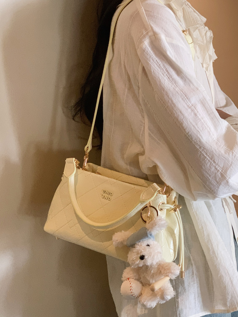 Cream quilted shoulder handbag with teddy bear charm worn with a white blouse