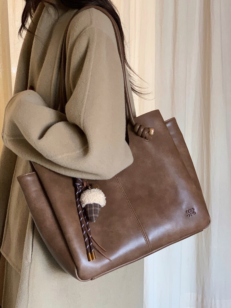 Brown leather tote bag worn on a model with a decorative charm