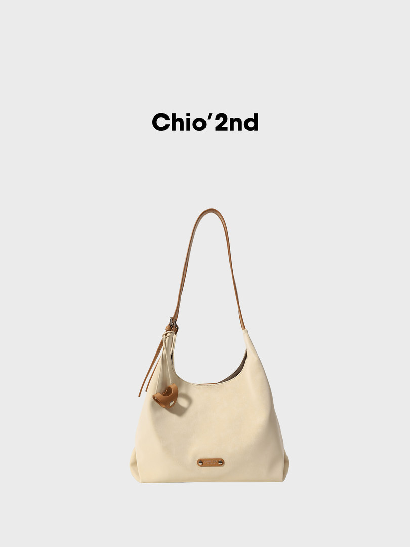 Cream shoulder handbag with brown strap and logo charm on a white background