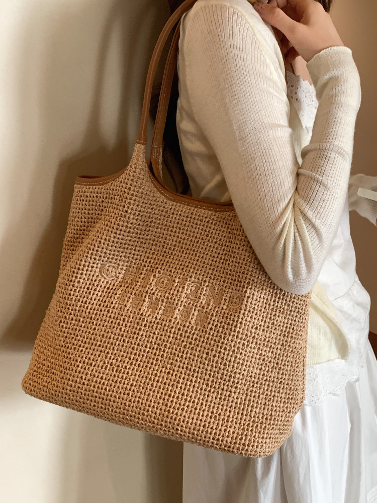 Woven straw tote bag worn by a person in a light outfit