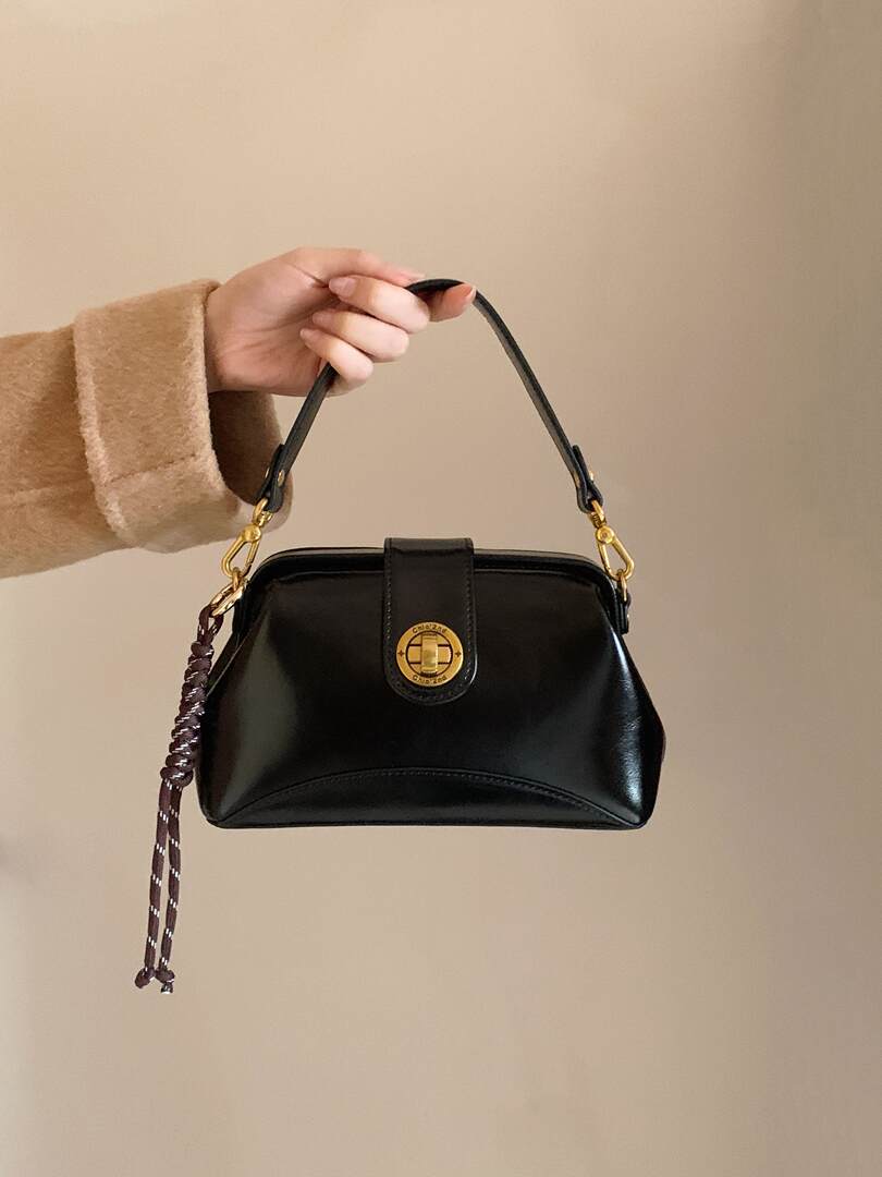 Black leather handbag with gold hardware held by hand