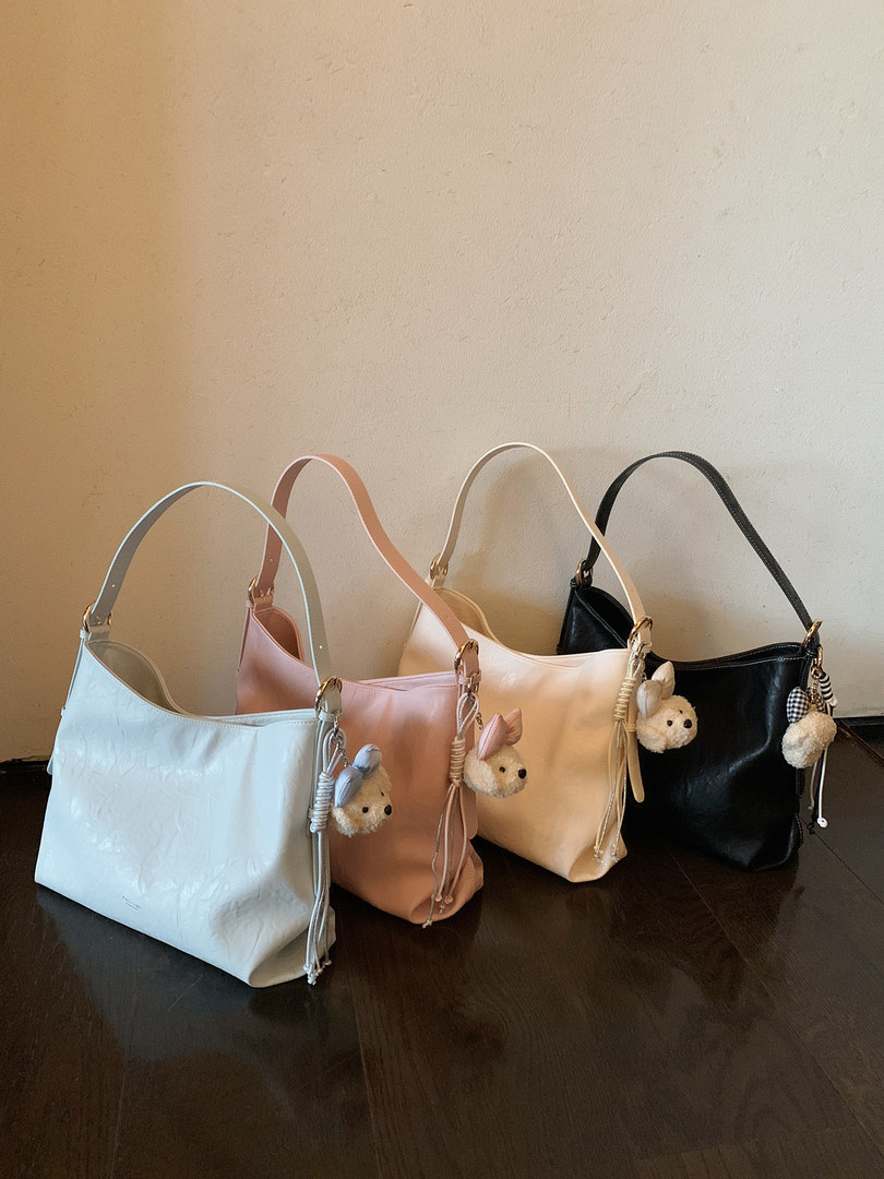 Four small shoulder handbags in pastel blue, pink, cream, and black displayed on a table