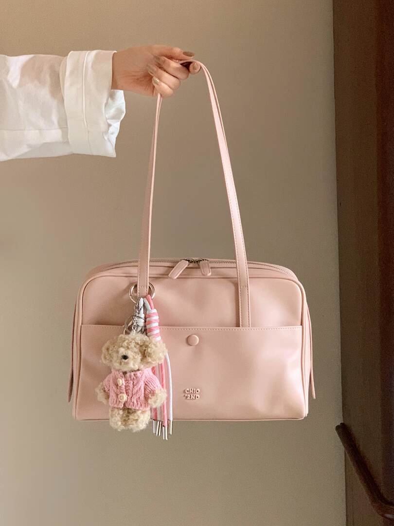 Pink shoulder handbag with a teddy keychain being held up by hand