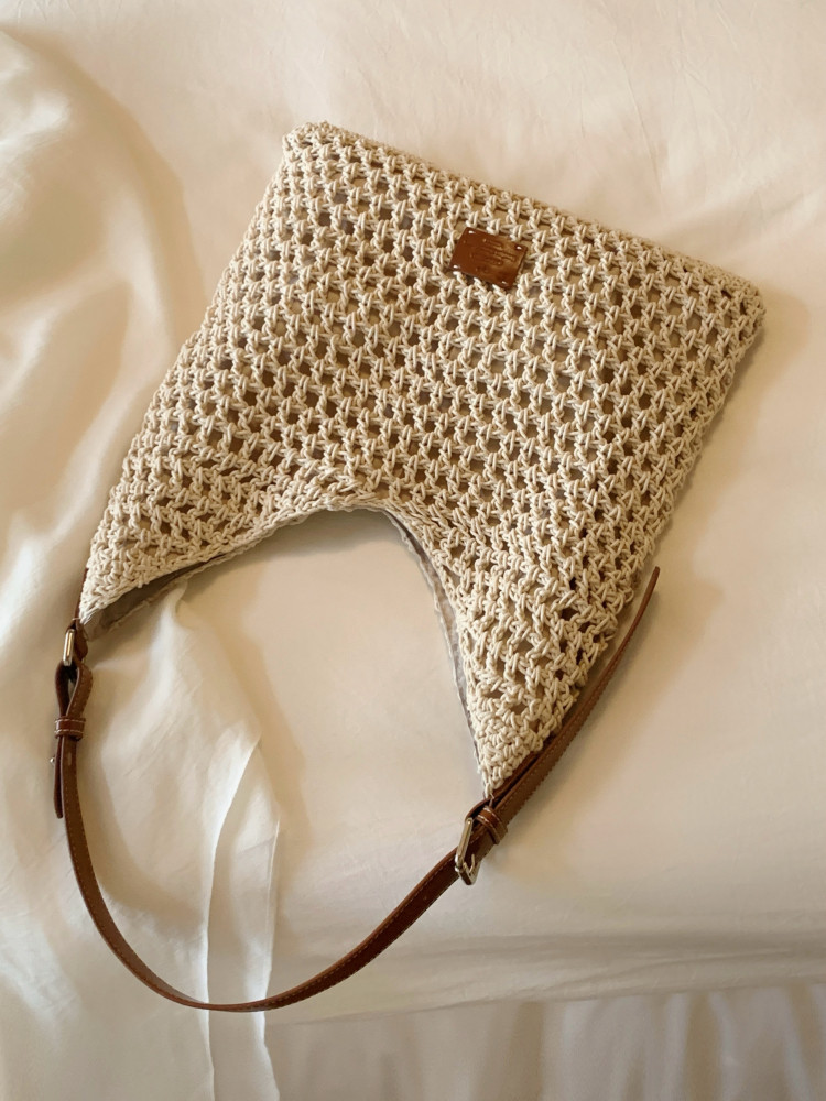 Beige woven crochet handbag with brown strap on a light fabric background