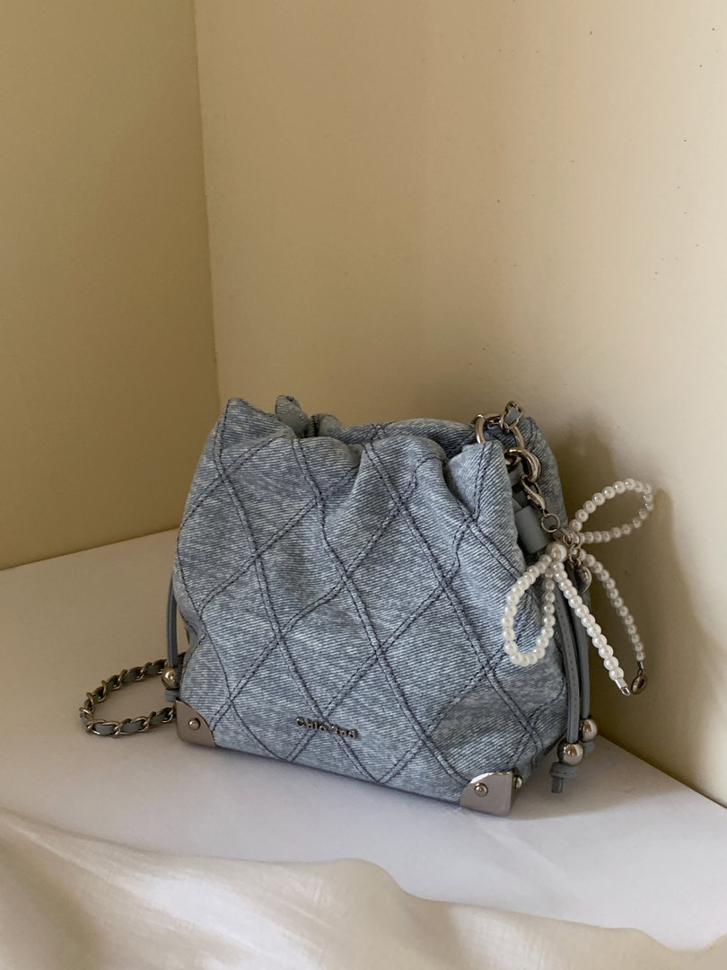 Quilted light blue handbag with chain and pearl strap on a shelf